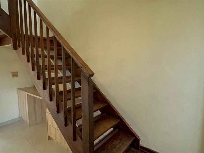 A functional hallway area featuring a wooden staircase with a matching balustrade and convenient built-in cabinetry integrated into the under-stair space.