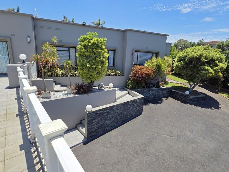 A well-maintained rear exterior featuring a tiled patio, stone-clad retaining walls, and a paved driveway area with established landscaping.