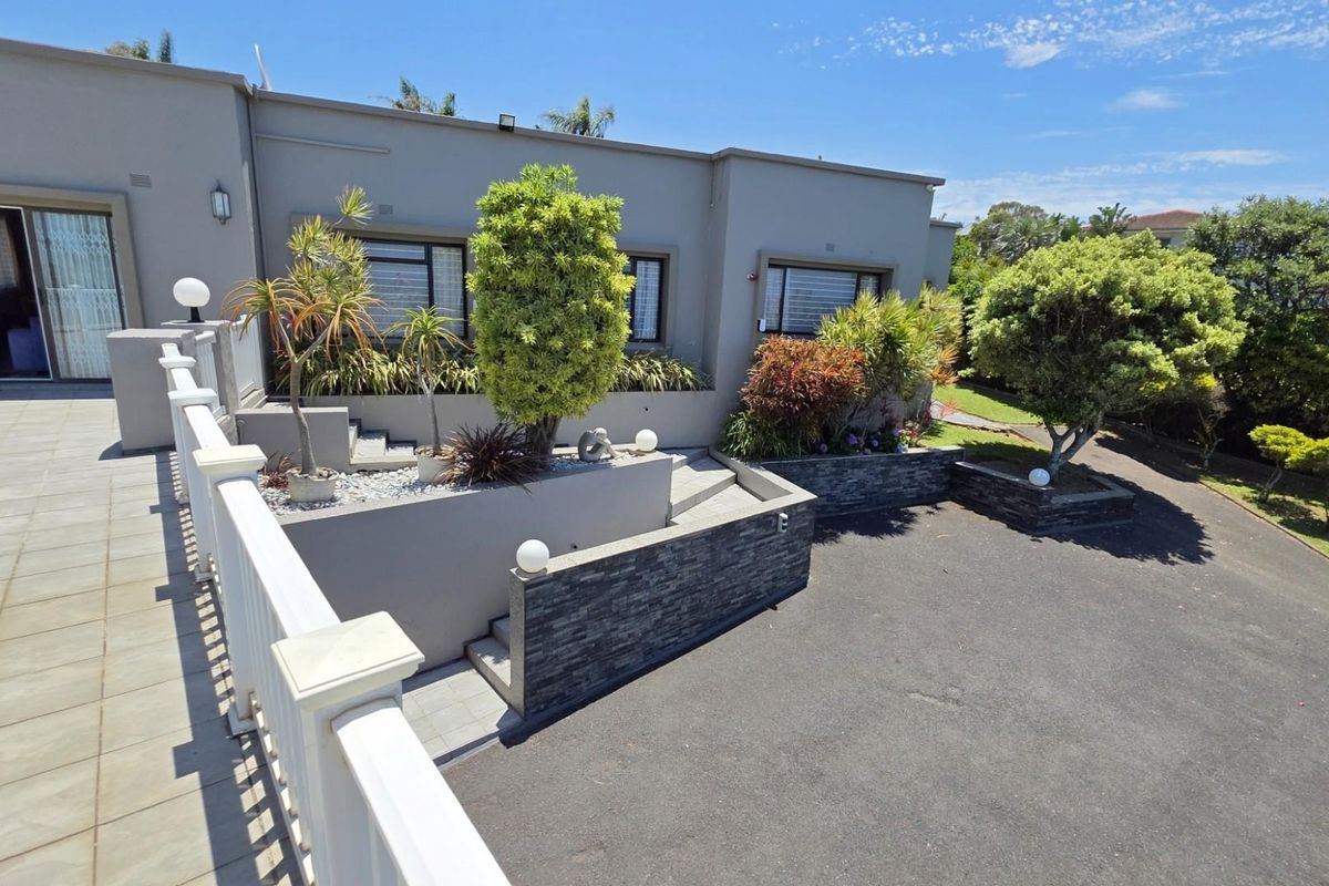 A well-maintained rear exterior featuring a tiled patio, stone-clad retaining walls, and a paved driveway area with established landscaping.