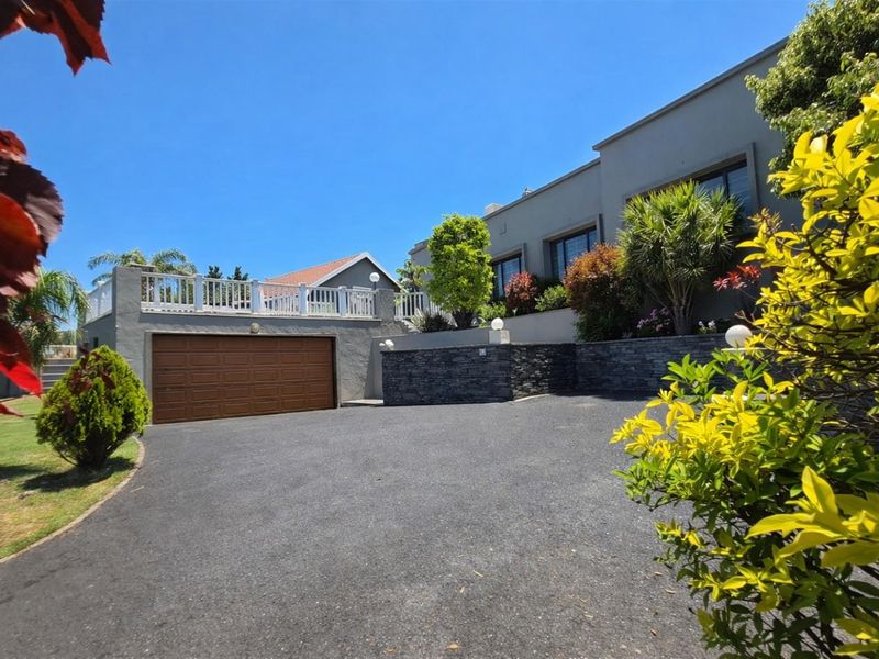 Front exterior view of the property featuring a paved driveway, a double garage, and an elevated balcony with stone-clad retaining walls.