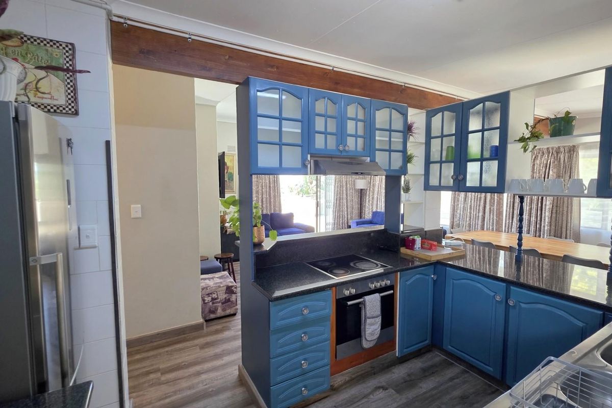 A functional kitchen featuring blue cabinetry, granite countertops, integrated oven and hob, and an open-plan layout connecting to the living area.