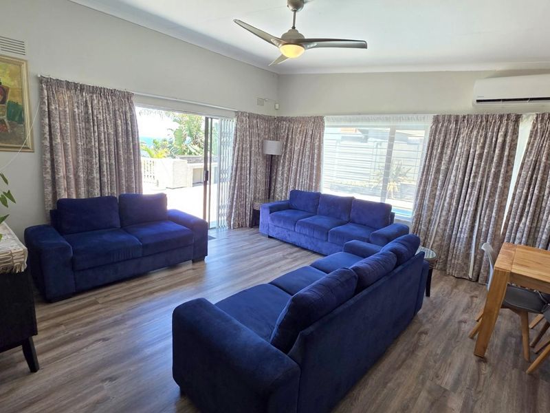 Spacious living room featuring laminate flooring, a ceiling fan, split-system air conditioning, and large sliding glass doors providing access to the outdoor area.