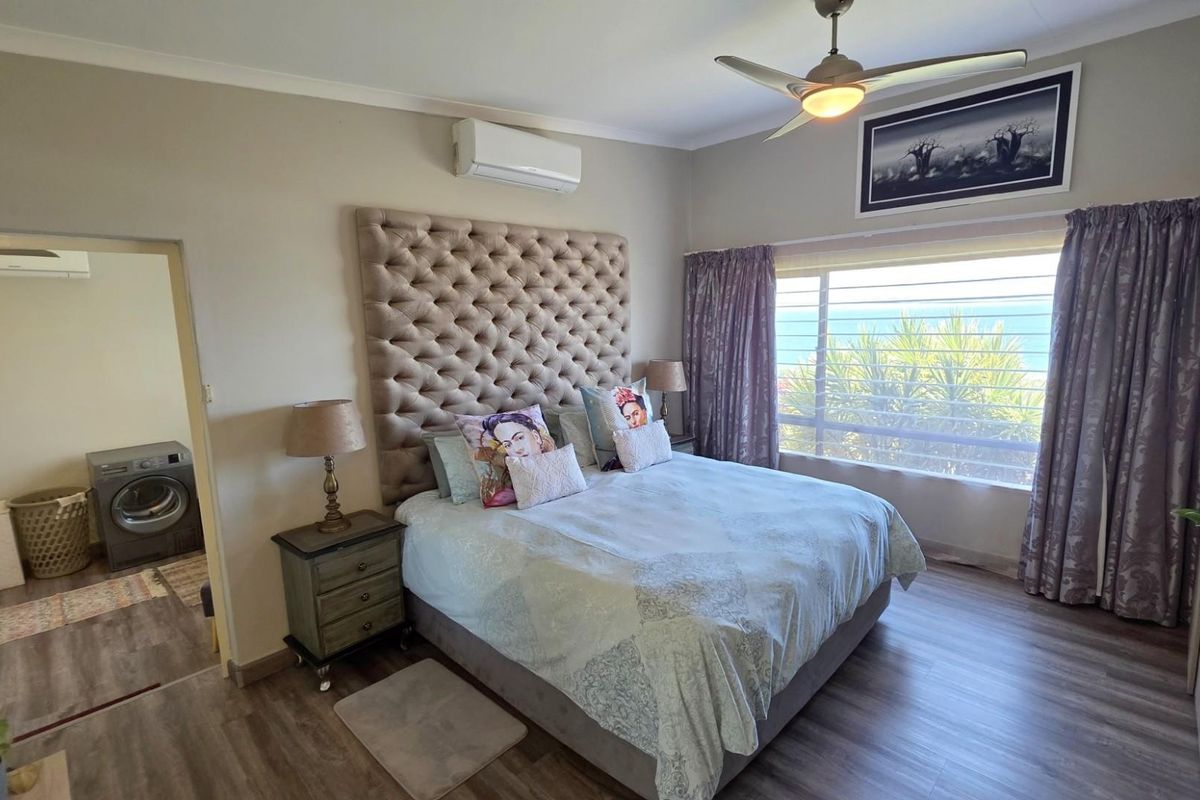 A well-maintained bedroom featuring laminate flooring, a ceiling fan, and a split-system air conditioner, with an adjoining utility space visible.
