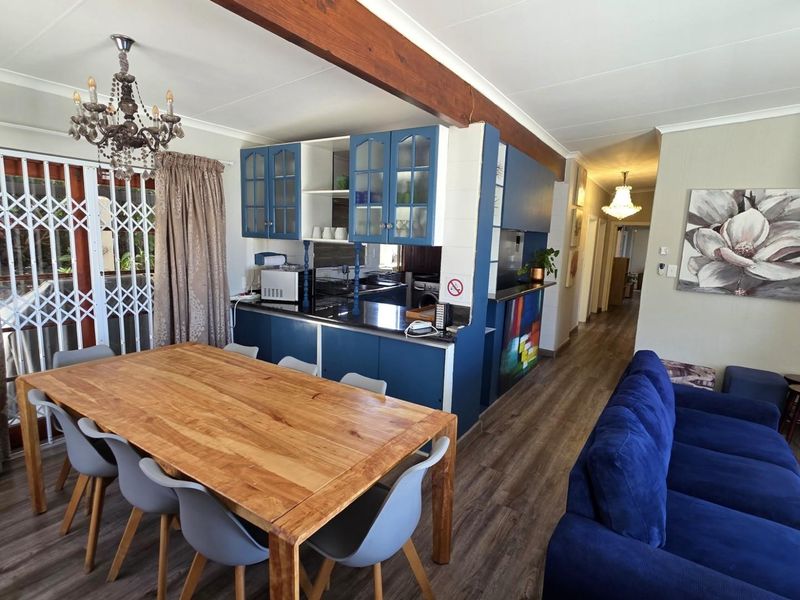 Open-plan living and dining area featuring laminate flooring, exposed timber beam, and a functional kitchen with blue cabinetry.