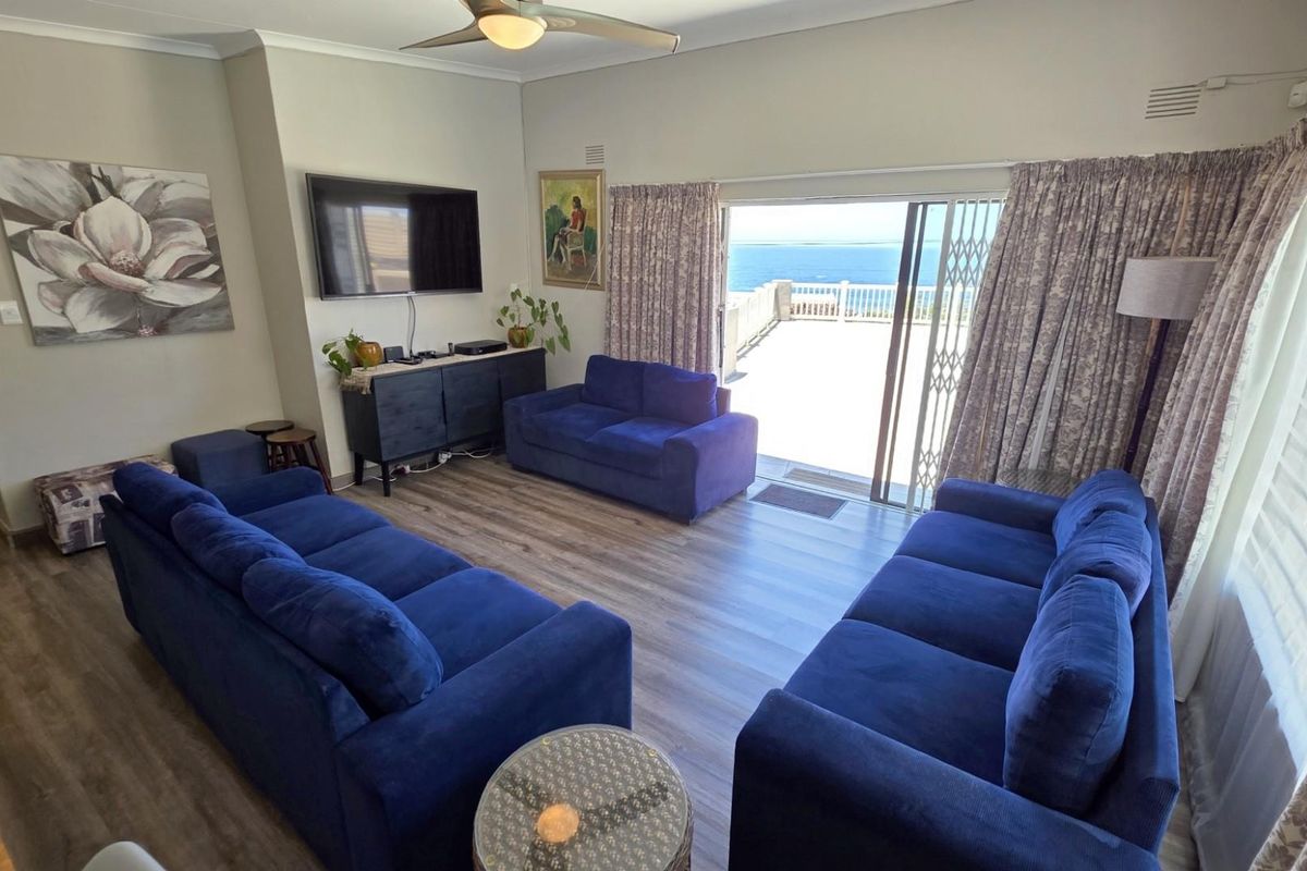 Spacious living room featuring laminate flooring, a ceiling fan, and large sliding glass doors that open onto a patio with ocean views.
