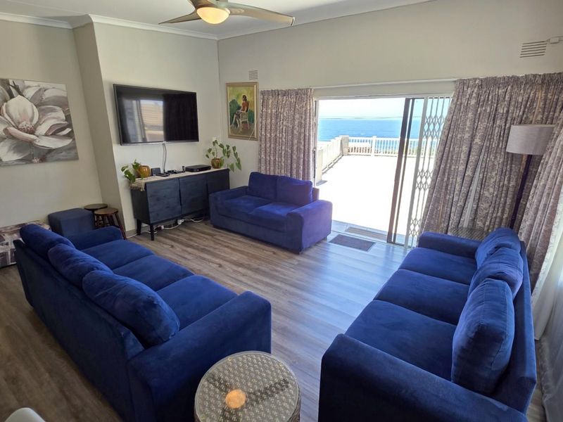 Spacious living room featuring laminate flooring, a ceiling fan, and large sliding glass doors that open onto a patio with ocean views.