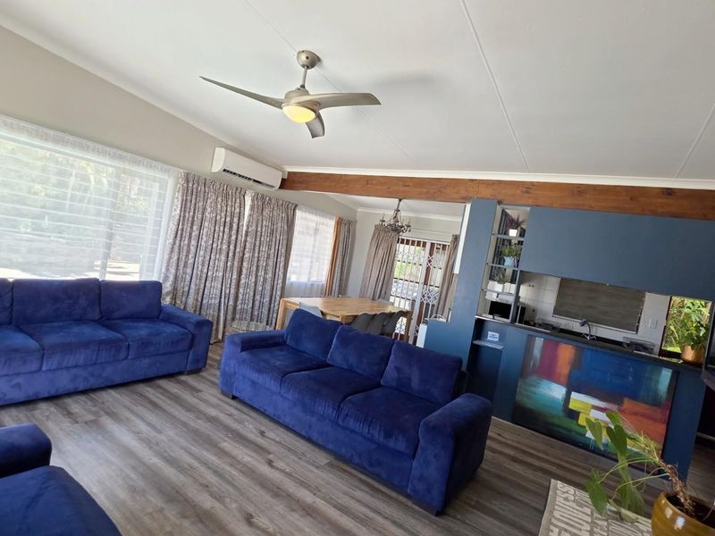Spacious open-plan living and dining area featuring modern laminate flooring, a ceiling fan, split-system air conditioning, and an exposed timber beam detail.