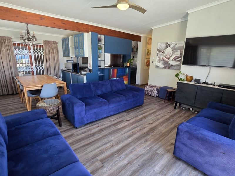 Spacious open-plan living and dining area featuring laminate flooring, an exposed timber beam, and a functional kitchen with blue cabinetry.