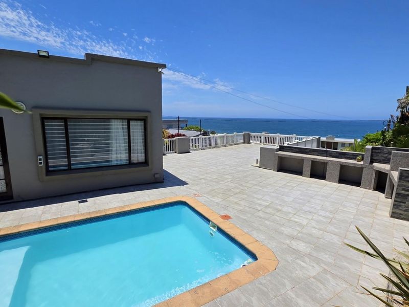 Spacious outdoor pool area featuring a tiled patio, built-in braai, and stunning ocean views, perfect for entertaining.