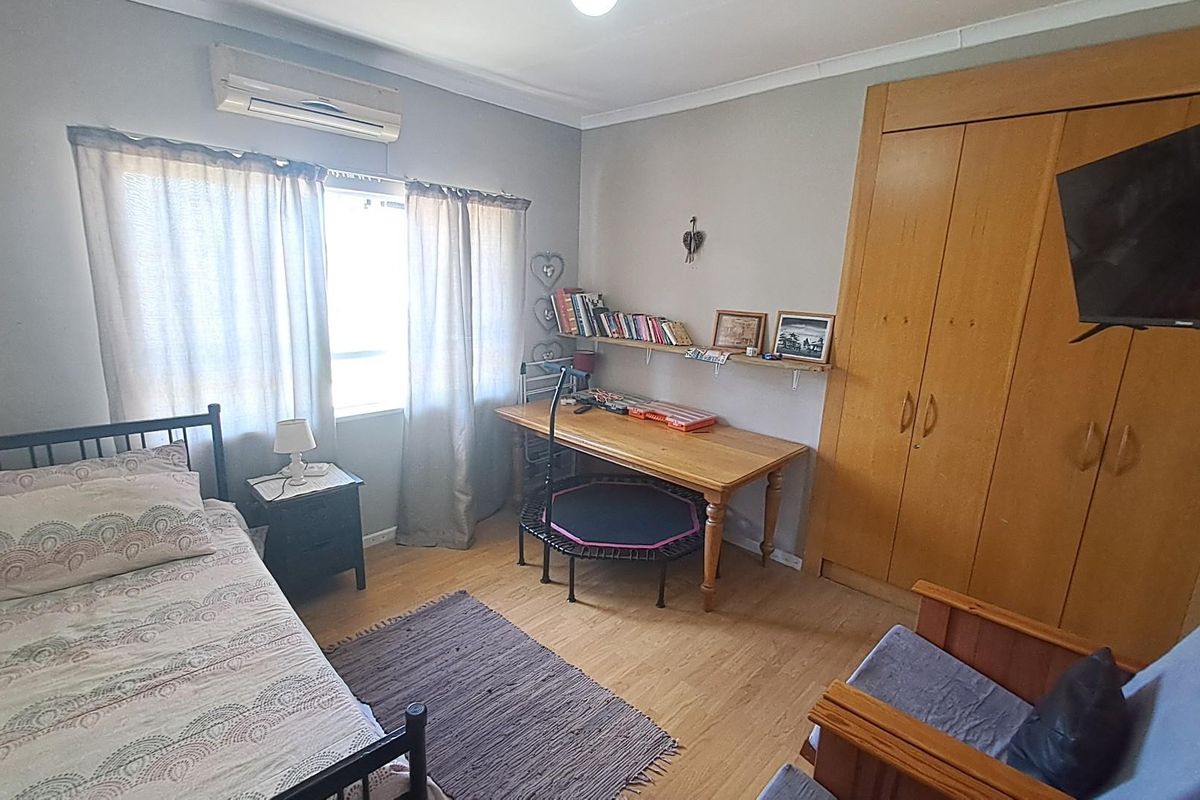 A functional bedroom featuring built-in wooden cupboards, laminate flooring, and a wall-mounted air conditioning unit.