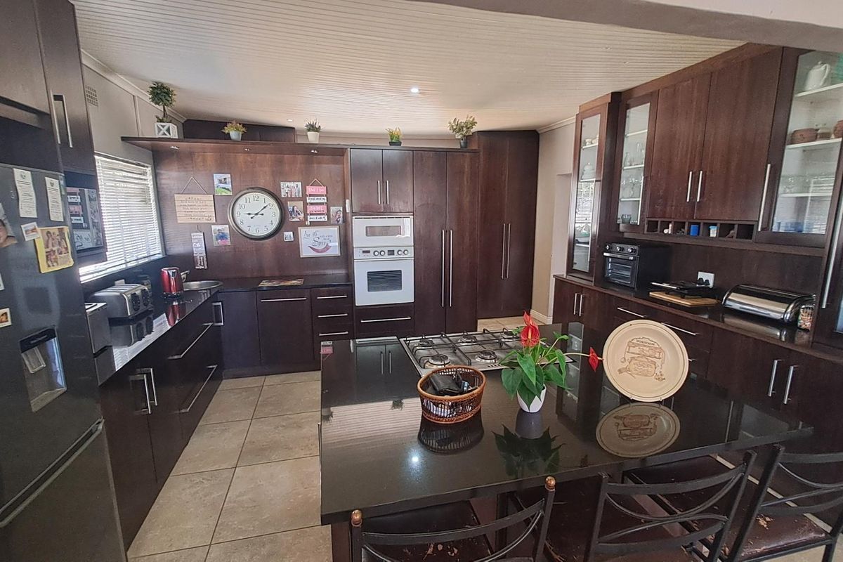 Spacious kitchen featuring dark wood cabinetry, granite countertops, a central island with a built-in gas hob, and integrated wall ovens.