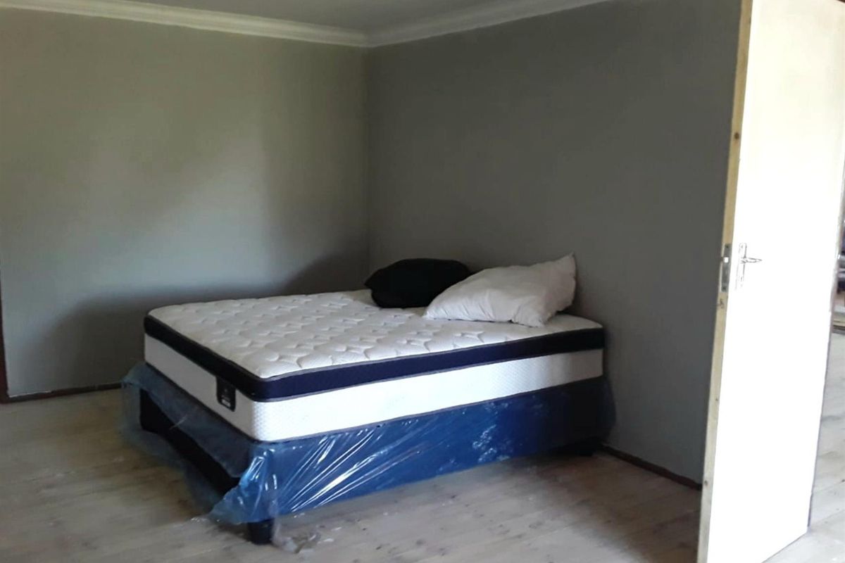 A simple bedroom featuring neutral grey walls and light-toned flooring, providing a blank canvas for personalization.