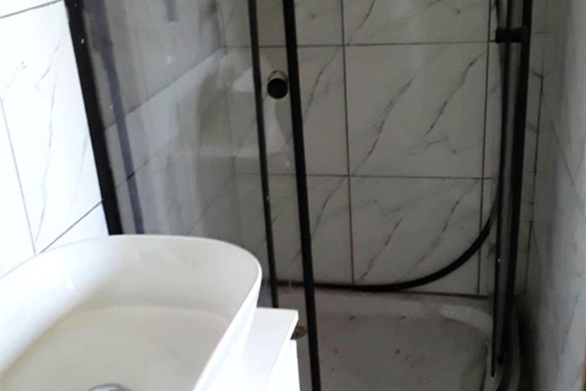 Compact bathroom featuring a modern vessel sink vanity and a corner shower enclosure with marble-look wall tiling.
