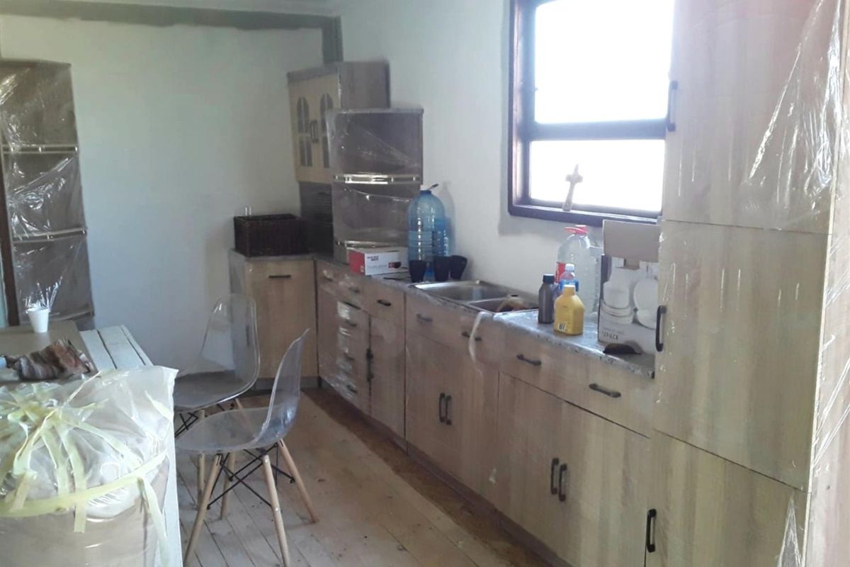 A kitchen area under construction featuring light wood-finish cabinetry, a stainless steel sink, and large windows, currently in an unfinished state.