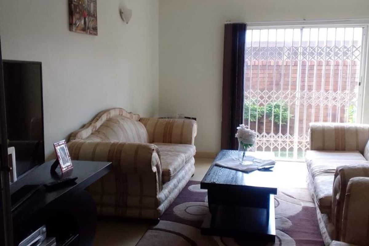 A living room featuring tiled flooring and a sliding glass door with security gate leading to an outdoor area.