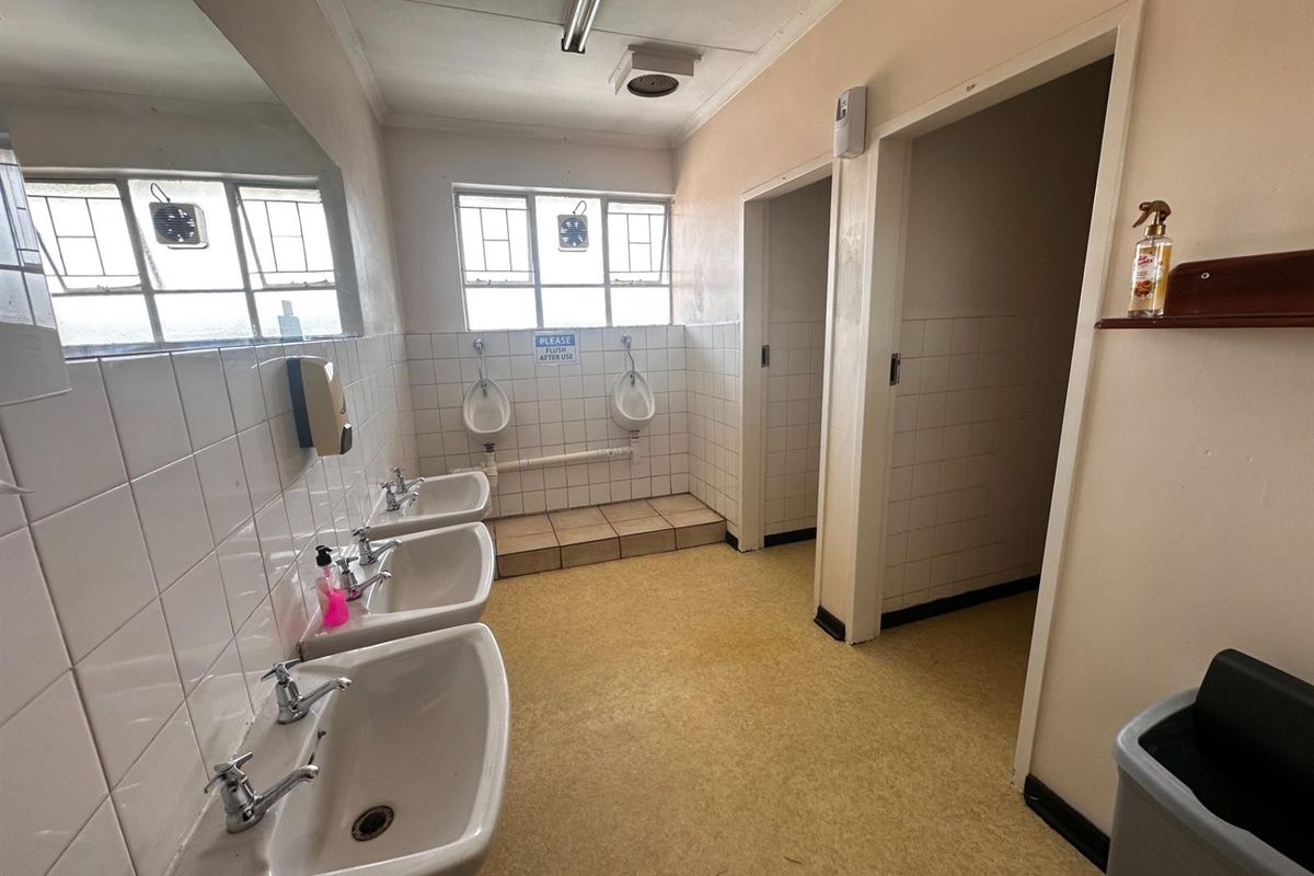 A functional commercial restroom facility featuring multiple wall-mounted basins, urinals, and separate toilet cubicles with basic finishes.