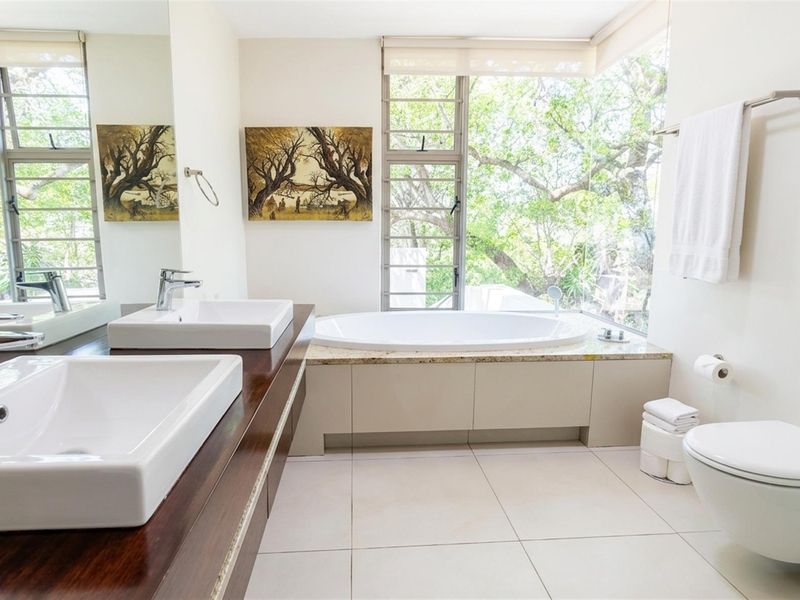 Modern bathroom featuring a double vanity with granite countertop, a built-in bathtub, and large windows offering natural light and garden views.