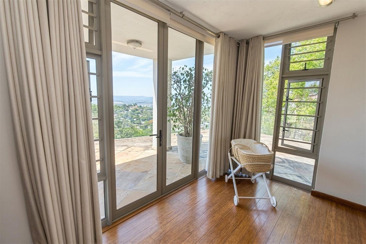Bright living area featuring expansive aluminium glass doors opening onto a patio with scenic elevated views and warm timber flooring.