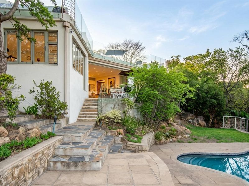 Rear exterior view featuring a swimming pool, stone staircase, paved patio area, and glass balustrades leading to the upper level.