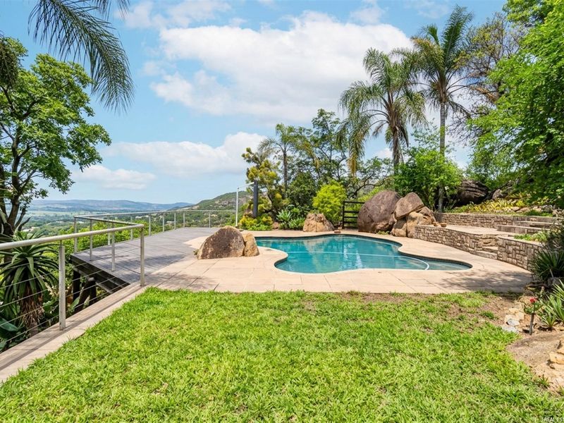 An outdoor pool area featuring a swimming pool, stone retaining walls, timber decking, and a metal balustrade with scenic landscape views.