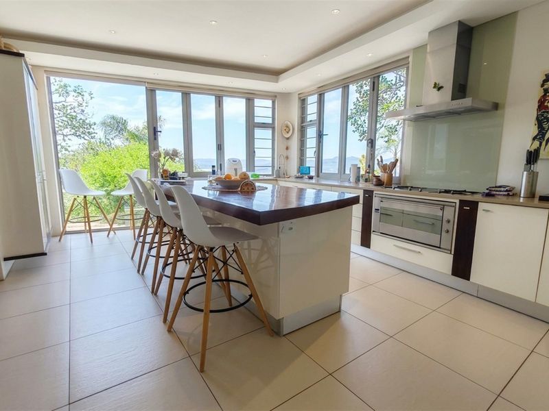 Modern kitchen featuring a central island, built-in oven, gas hob, and large windows offering natural light and scenic views.