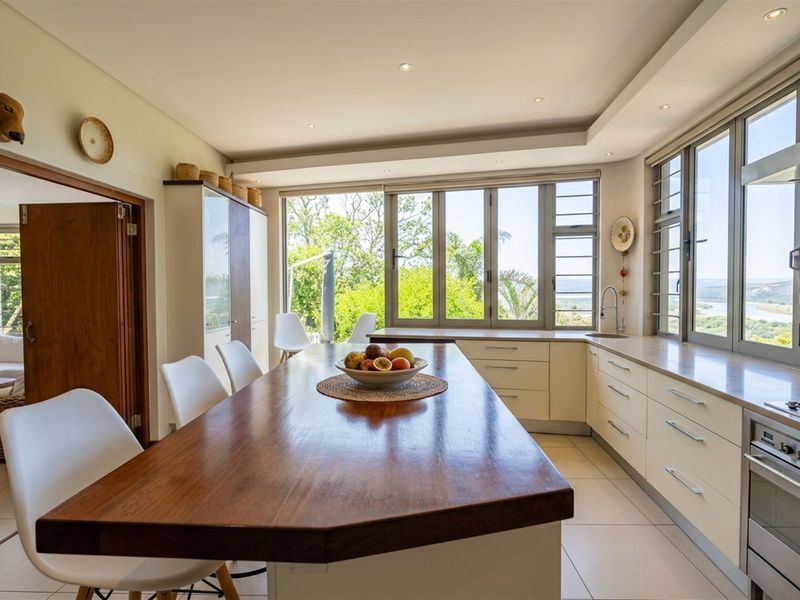 Modern kitchen featuring a large wooden island, built-in appliances, tiled flooring, and expansive windows offering scenic views.