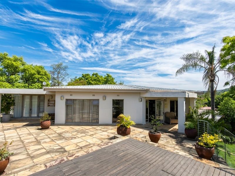 Spacious rear patio featuring a combination of paved and timber decking, glass balustrades, and direct access to the home through multiple sliding doors.