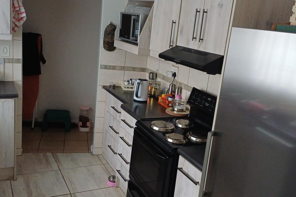A functional kitchen featuring light wood-grain cabinetry, tiled splashbacks, a built-in extractor fan, and a freestanding stove.