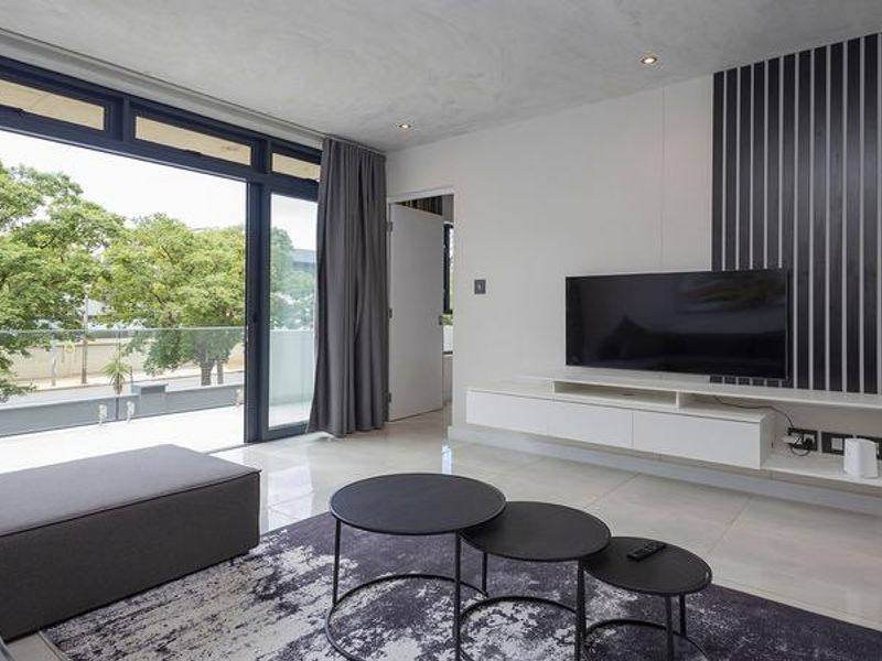 Modern living room featuring sleek tiled floors, recessed lighting, a wall-mounted media console, and large sliding doors opening to a balcony with a glass balustrade.