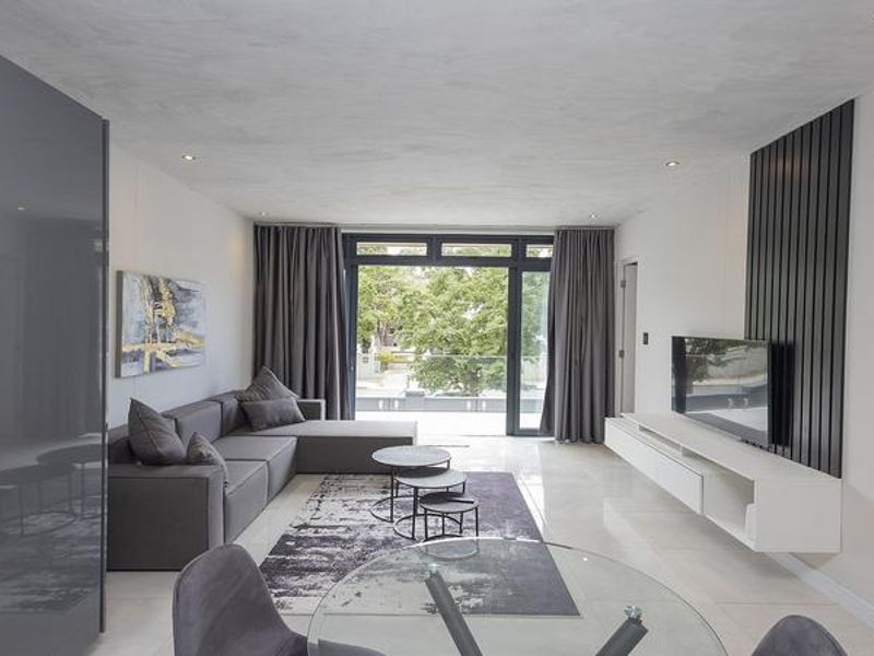 Modern open-plan living area featuring sleek built-in cabinetry, a floating media console with slatted wall detail, and large sliding doors leading to a balcony.