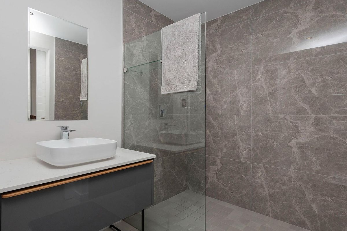 Modern bathroom featuring a floating vanity with a vessel sink, large-format marble-look wall tiles, and a frameless glass shower enclosure.