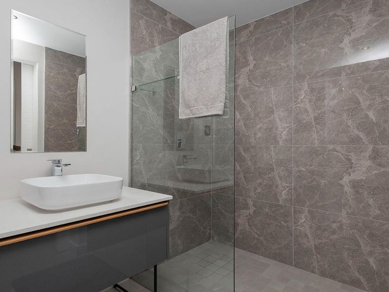 Modern bathroom featuring a floating vanity with a vessel sink, large-format marble-look wall tiles, and a frameless glass shower enclosure.