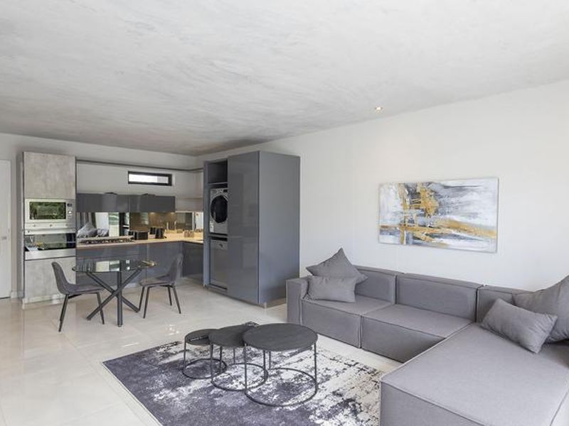 Modern open-plan living area featuring a sleek, integrated kitchen with built-in appliances, recessed lighting, and polished tiled flooring throughout.