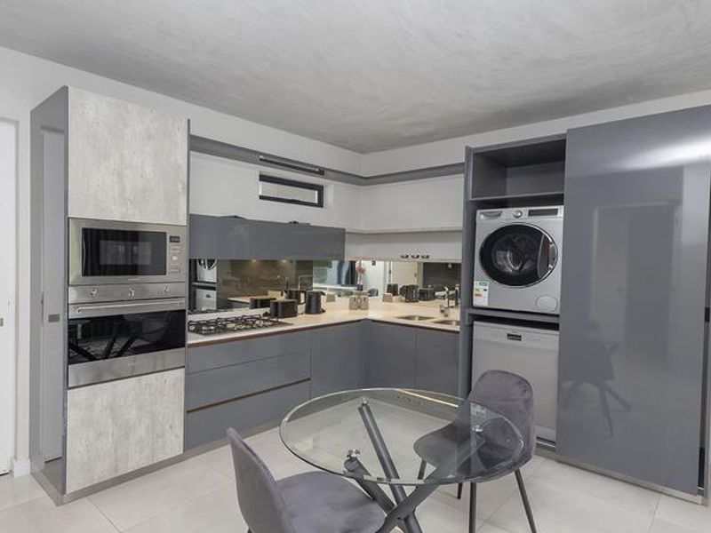 Modern kitchen featuring high-gloss cabinetry, integrated appliances including a laundry unit and dishwasher, built-in oven, microwave, and a sleek mirrored splashback.