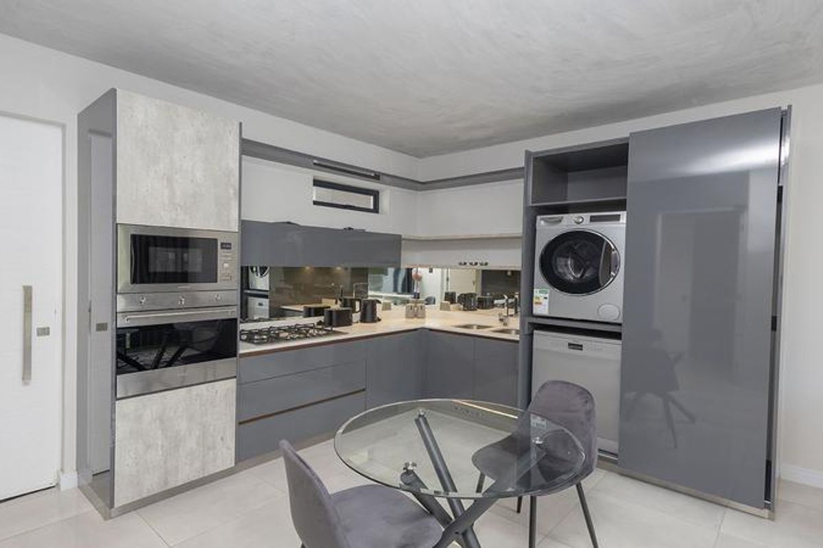 Modern kitchen featuring high-gloss cabinetry, integrated appliances including a laundry unit and dishwasher, built-in oven, microwave, and a sleek mirrored splashback.