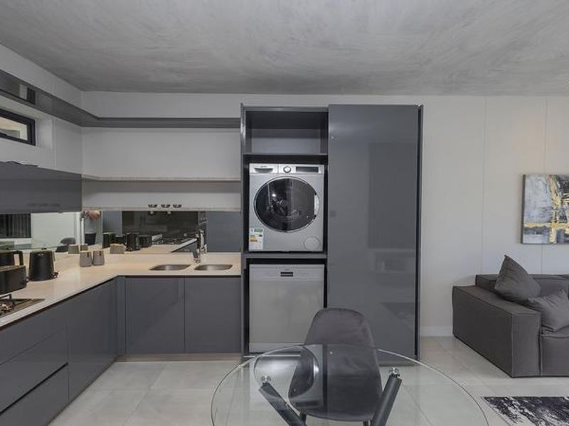 Modern open-plan kitchen featuring sleek grey cabinetry, integrated appliances, a gas hob, and a mirrored splashback, seamlessly flowing into the living area.