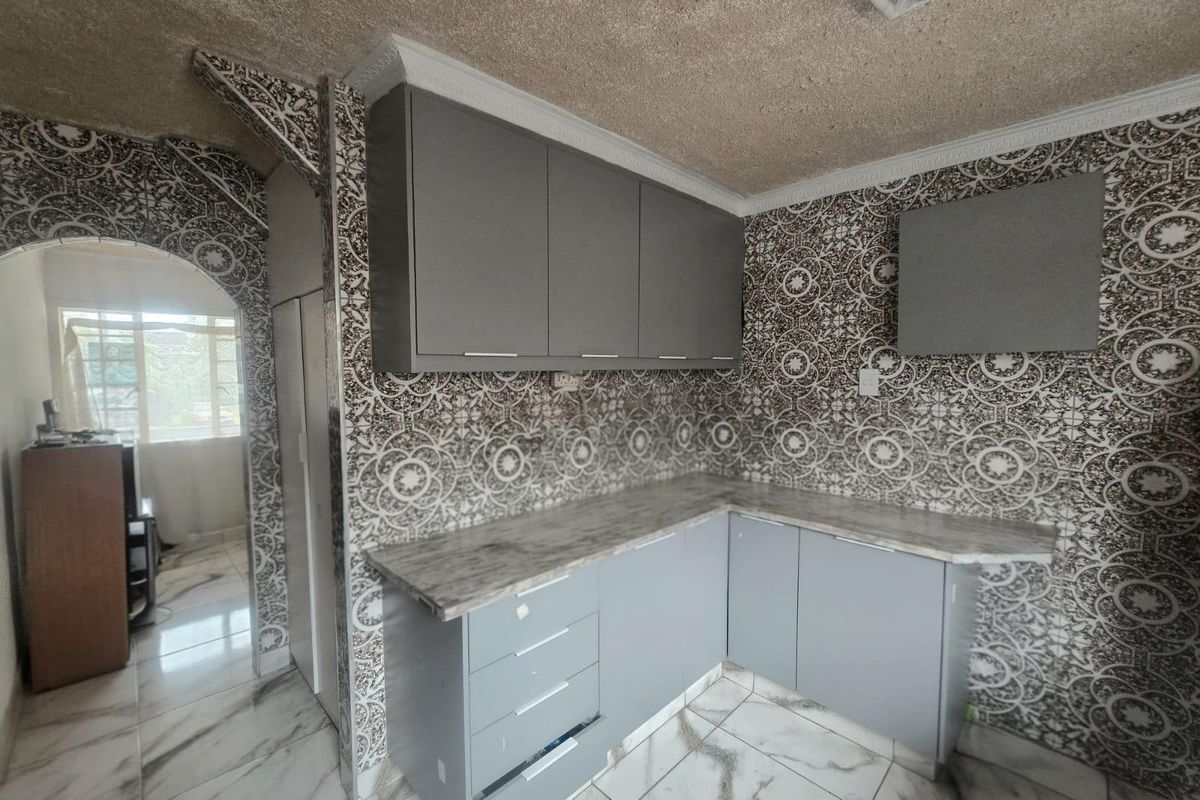 A compact kitchen featuring modern grey cabinetry, marble-effect countertops, and distinctive patterned wall tiling with an arched entrance.
