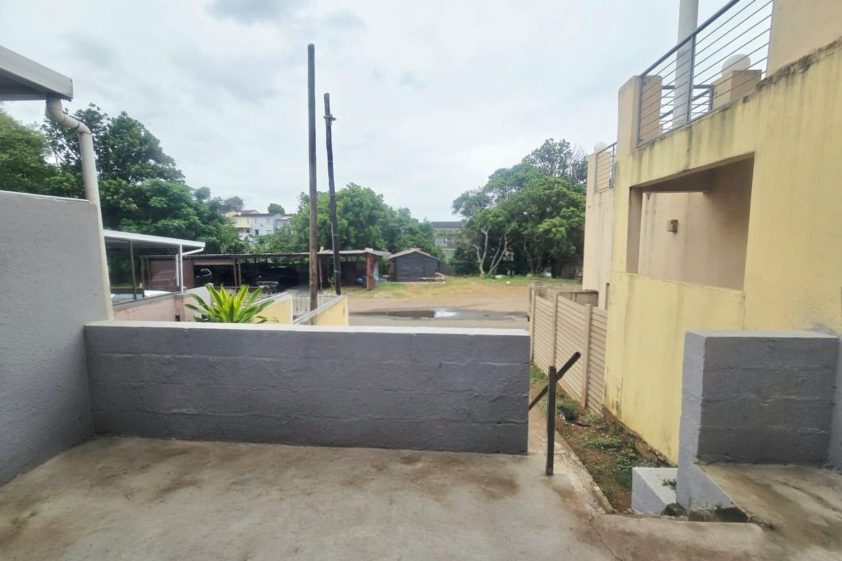 Rear exterior view showing a concrete patio area, masonry boundary walls, and metal railings leading to an outdoor space.