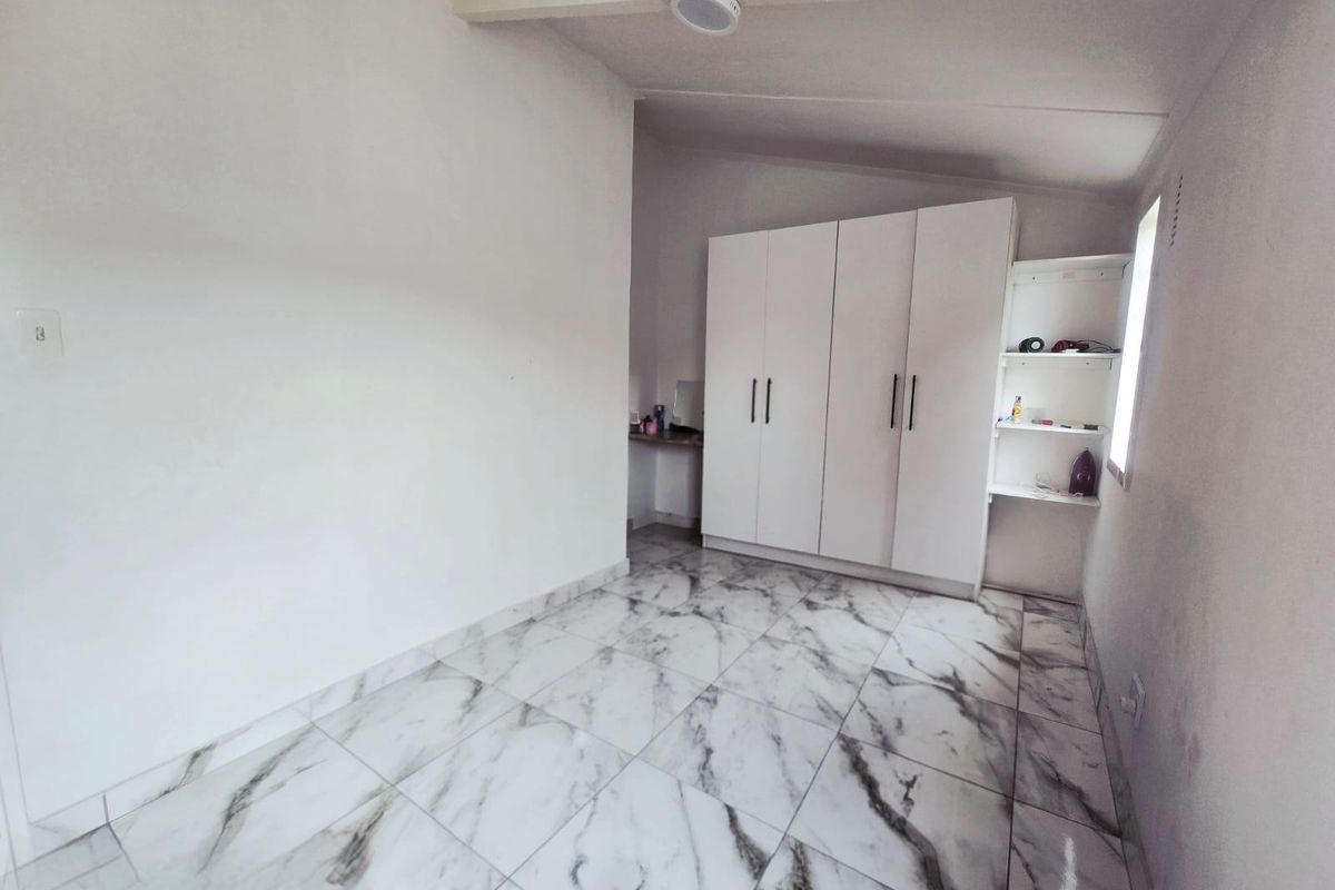A clean, empty bedroom featuring modern marble-look floor tiles and a white built-in wardrobe with integrated shelving.