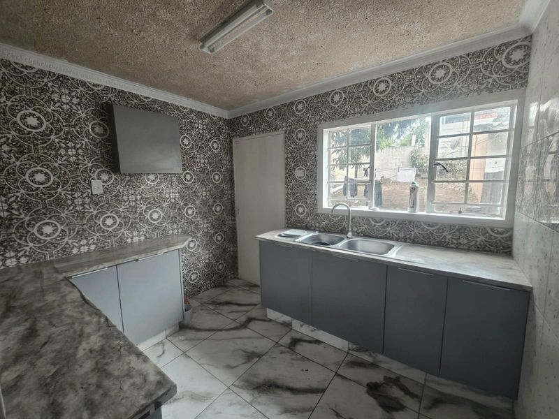 A functional kitchen featuring grey cabinetry, laminate countertops, a double sink, and distinctive patterned wall tiles with tiled flooring.
