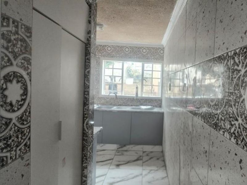 A functional scullery area featuring built-in cabinetry, a double sink, and decorative wall tiling with a distinct arched entryway.