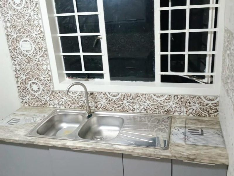 A functional kitchen area featuring a double bowl stainless steel sink, modern grey base cabinetry, and decorative patterned wall tiles.