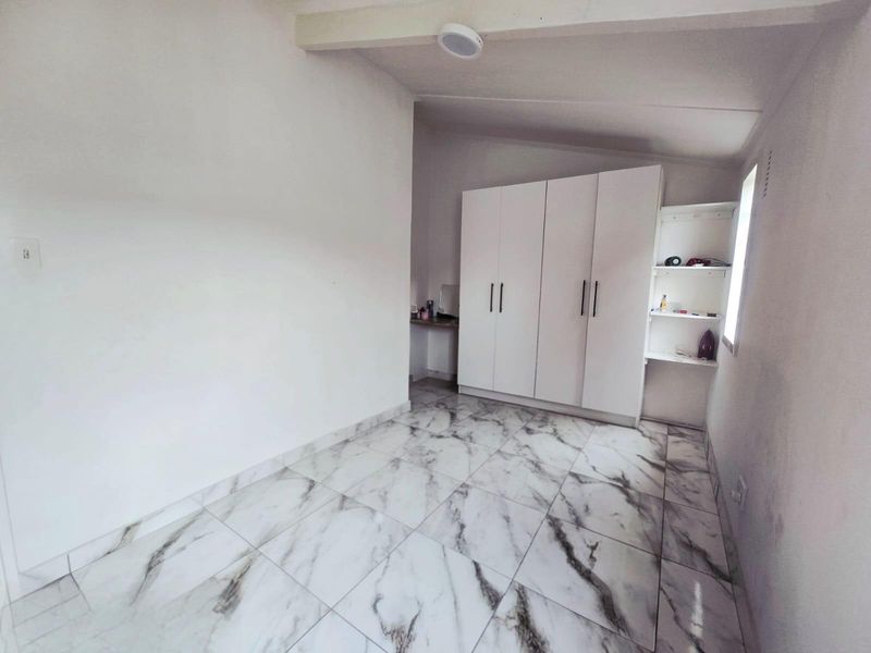 A clean, empty bedroom featuring modern marble-look floor tiles and a white built-in wardrobe with integrated shelving.