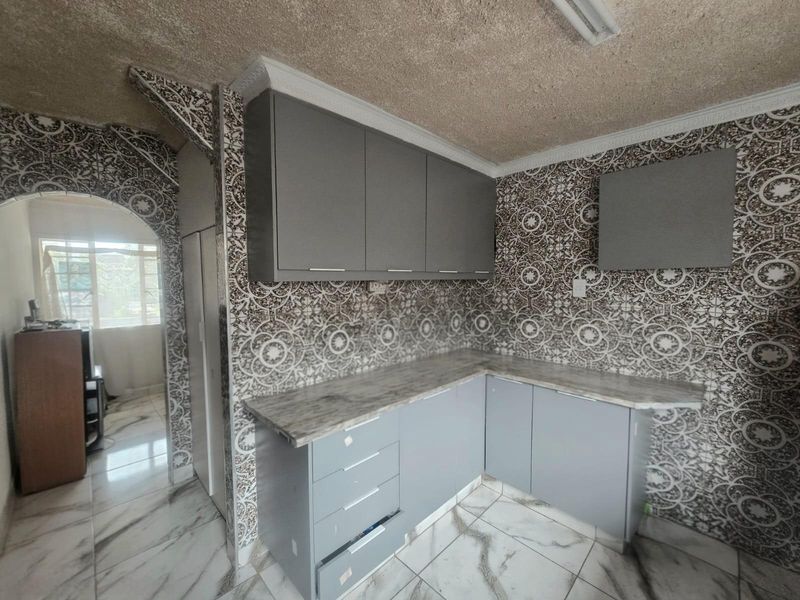 A compact kitchen featuring modern grey cabinetry, marble-effect countertops, and distinctive patterned wall tiling with an arched entrance.