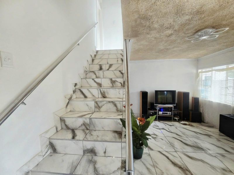 Living area featuring marble-effect floor tiles, a matching tiled staircase with a stainless steel handrail, and a textured ceiling finish.