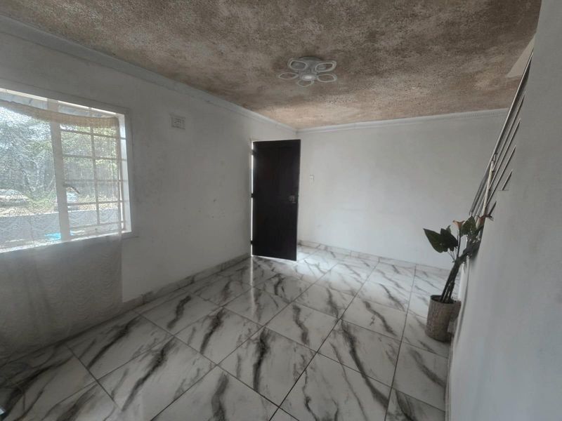 An empty living area featuring marble-look tiled flooring, a staircase with a metal railing, and a textured ceiling finish.