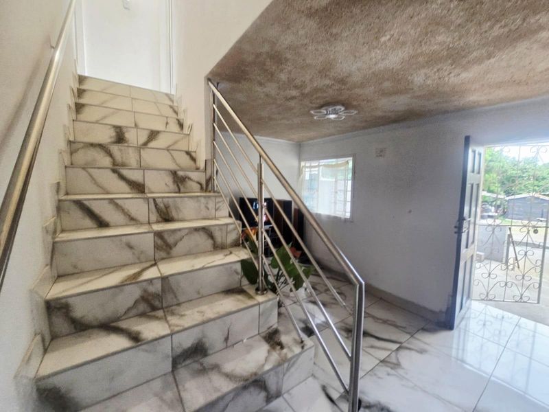 Entrance area featuring a marble-effect tiled staircase with a stainless steel balustrade, leading to an open living space with an unfinished ceiling.
