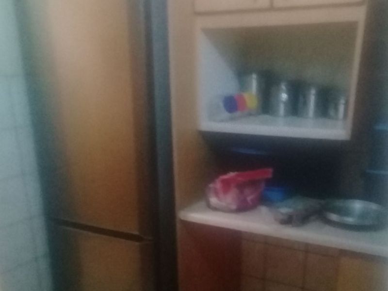 A small kitchen area featuring built-in cabinetry, tiled flooring, and a tiled backsplash, showing signs of age and wear.