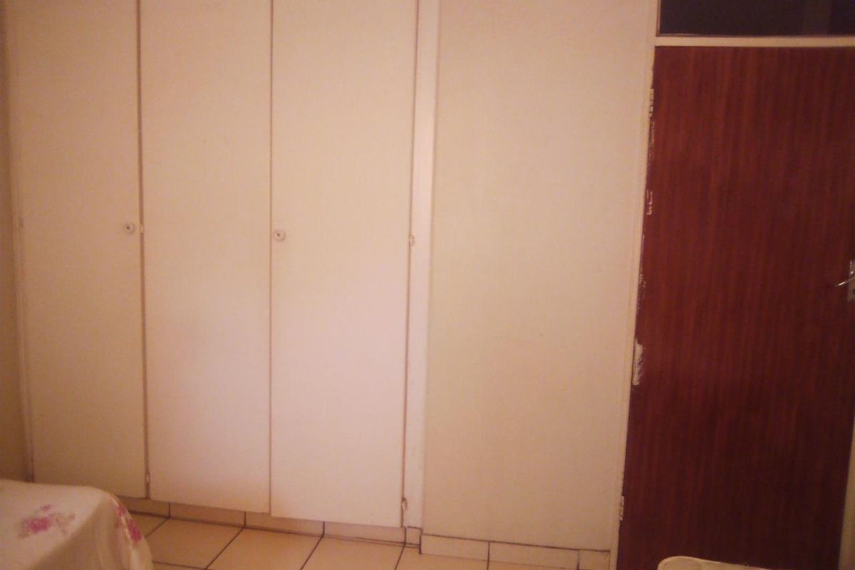 A bedroom featuring built-in cupboards with white doors and tiled flooring, providing functional storage space within the apartment.