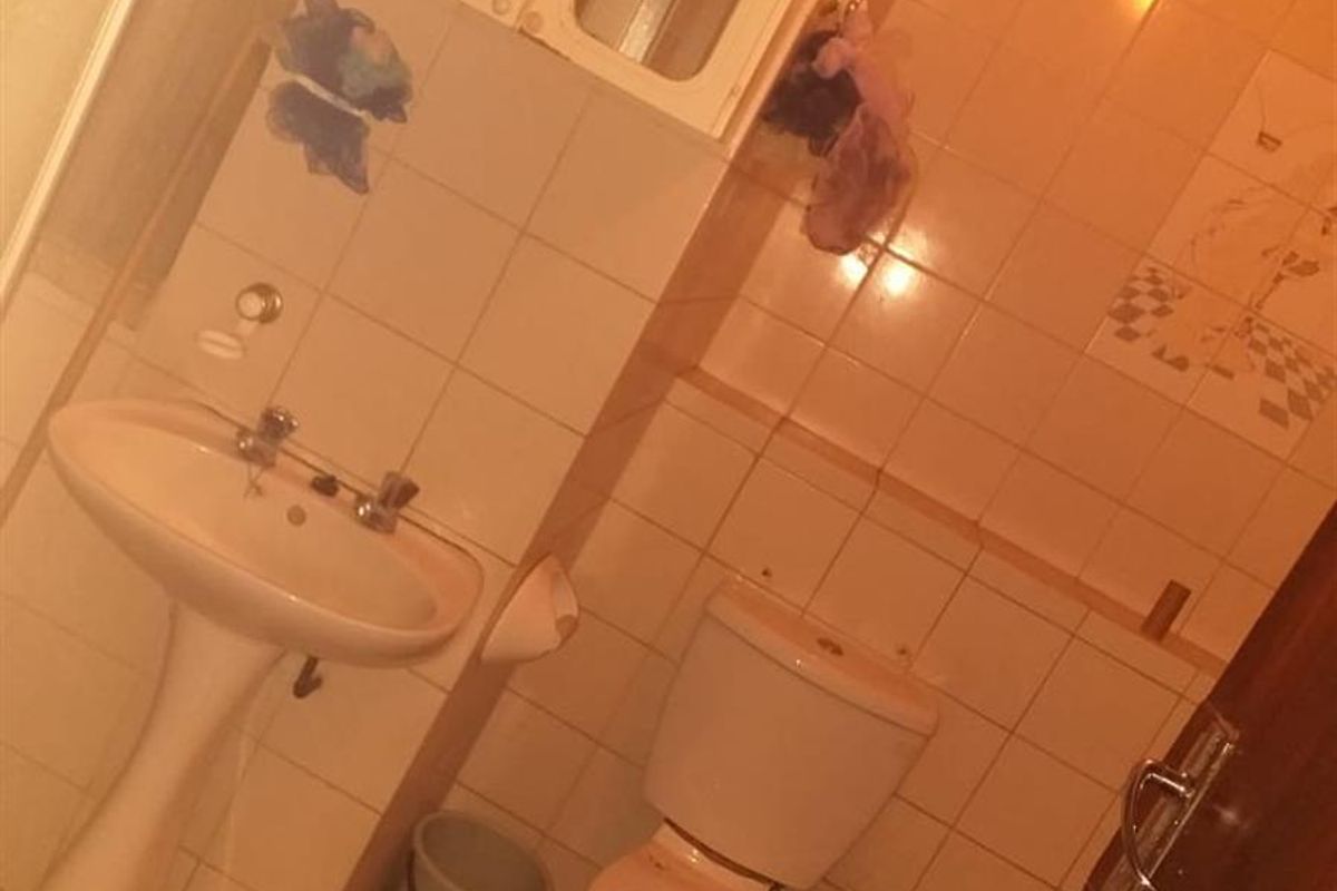 A dated bathroom featuring a pedestal sink, toilet, and wall-mounted medicine cabinet with tiled walls and flooring.